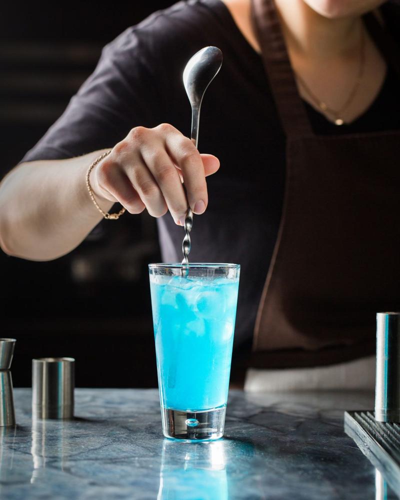 Bartender stirring a blue cocktail